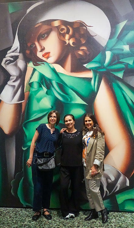 three women standing in front of a wall mural