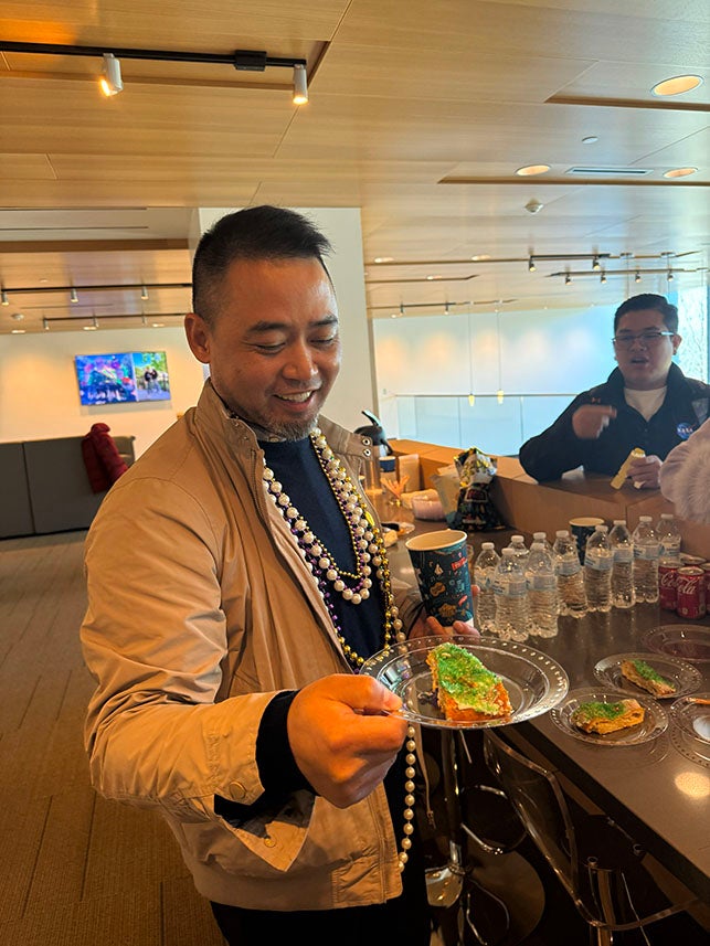 adult man holding a piece of king cake and smiling