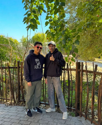 two young male adults posing in front of a rhino exhibit at a zoo