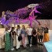 adults standing in a science museum in front of a dinosaur skeleton
